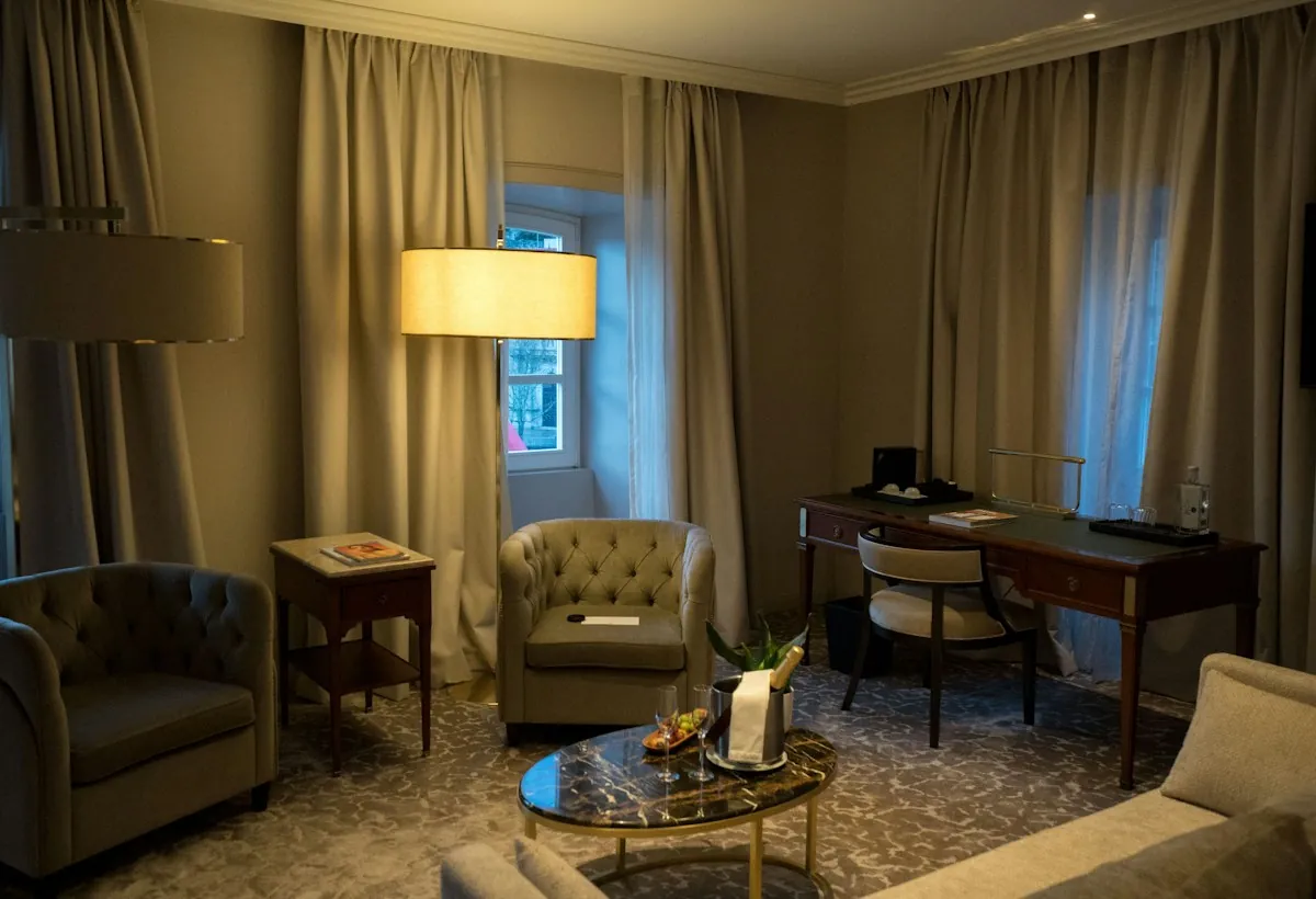A hotel suite with armchairs, a writing desk and lamps lit